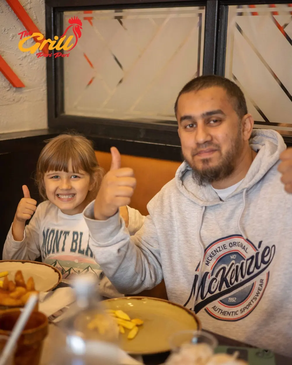 Father and young daughter giving thumbs up over a meal at The Grill Peri Peri, Mill Road