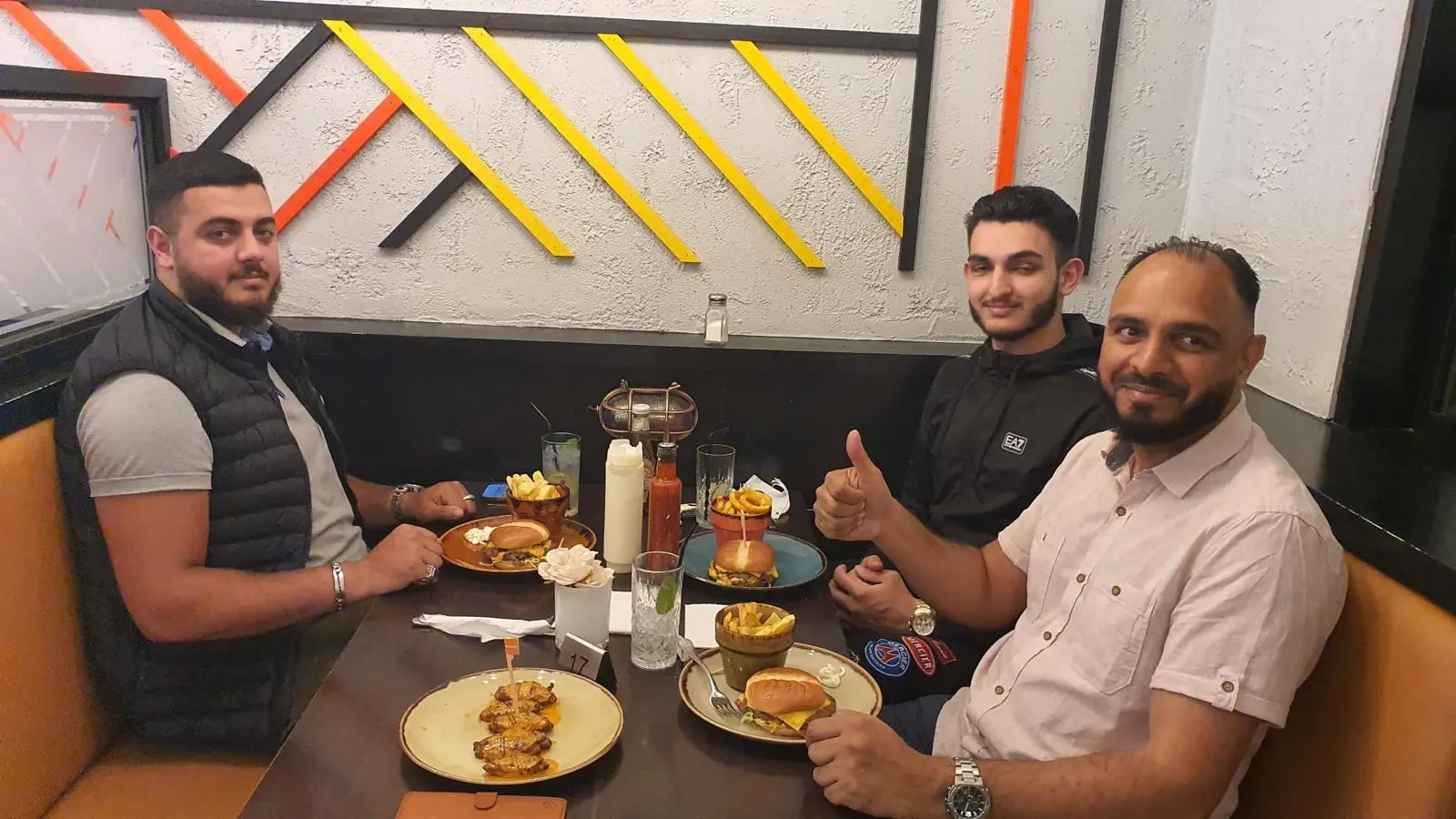 Three guests enjoying smash burgers, chicken skewers and fries in a booth at The Grill Peri Peri