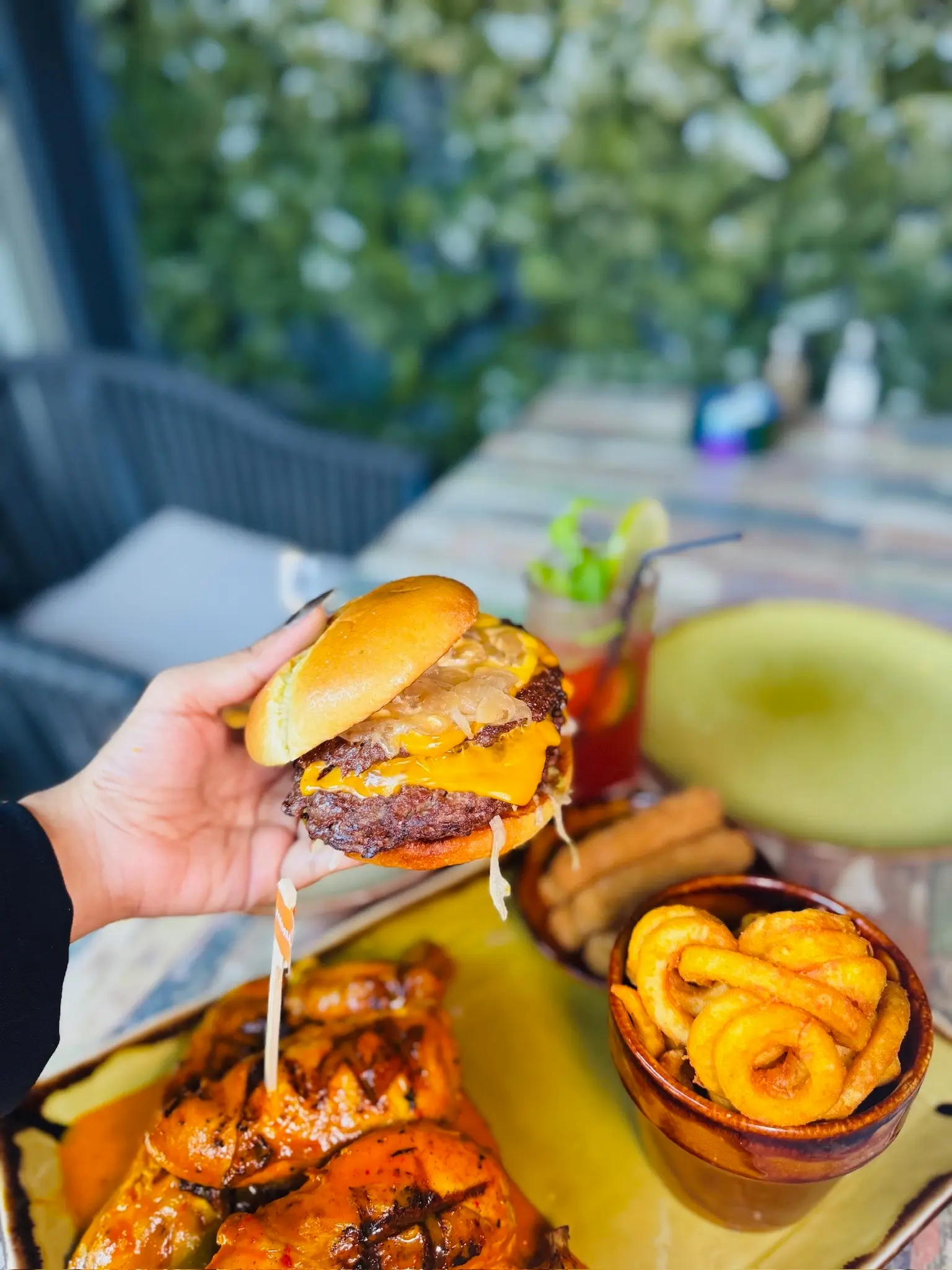 Hand holding a double cheeseburger with flame-grilled peri chicken, curly fries and mozzarella sticks